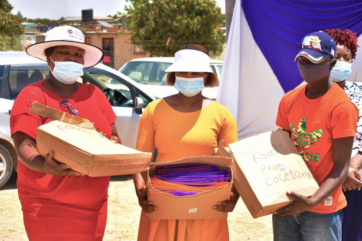 Three people stand together outdoors holding labeled cardboard boxes