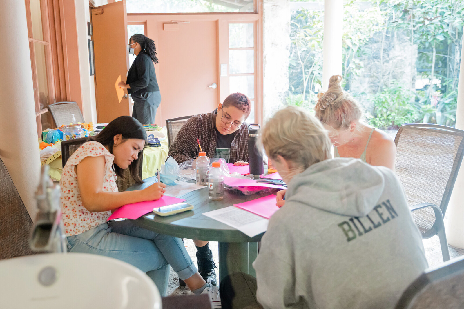 A group of young adults sit around a table together working on various projects.