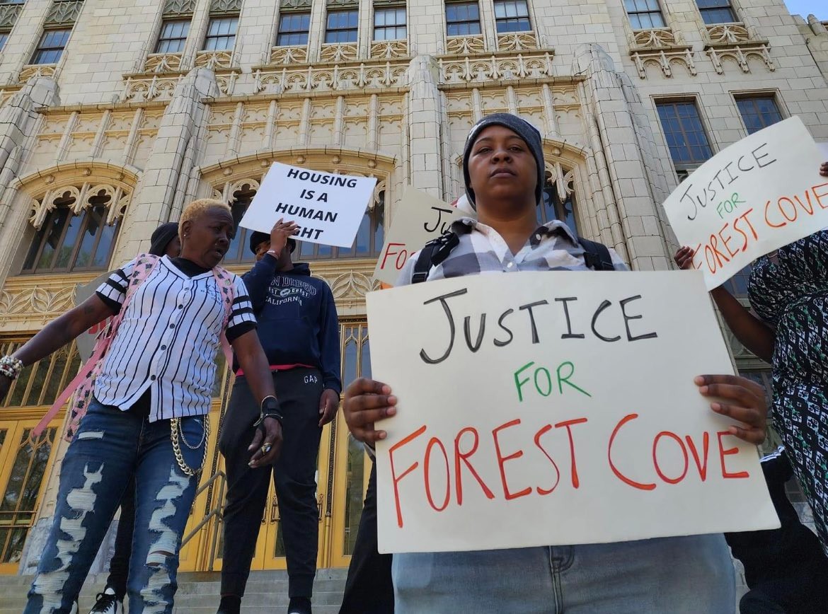 4 people hold signs in front of a high rise