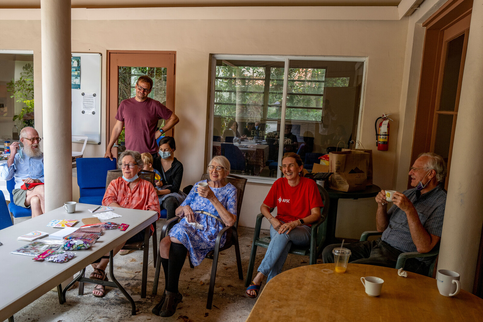 A group of people sit around several tables writing letters together and talking.