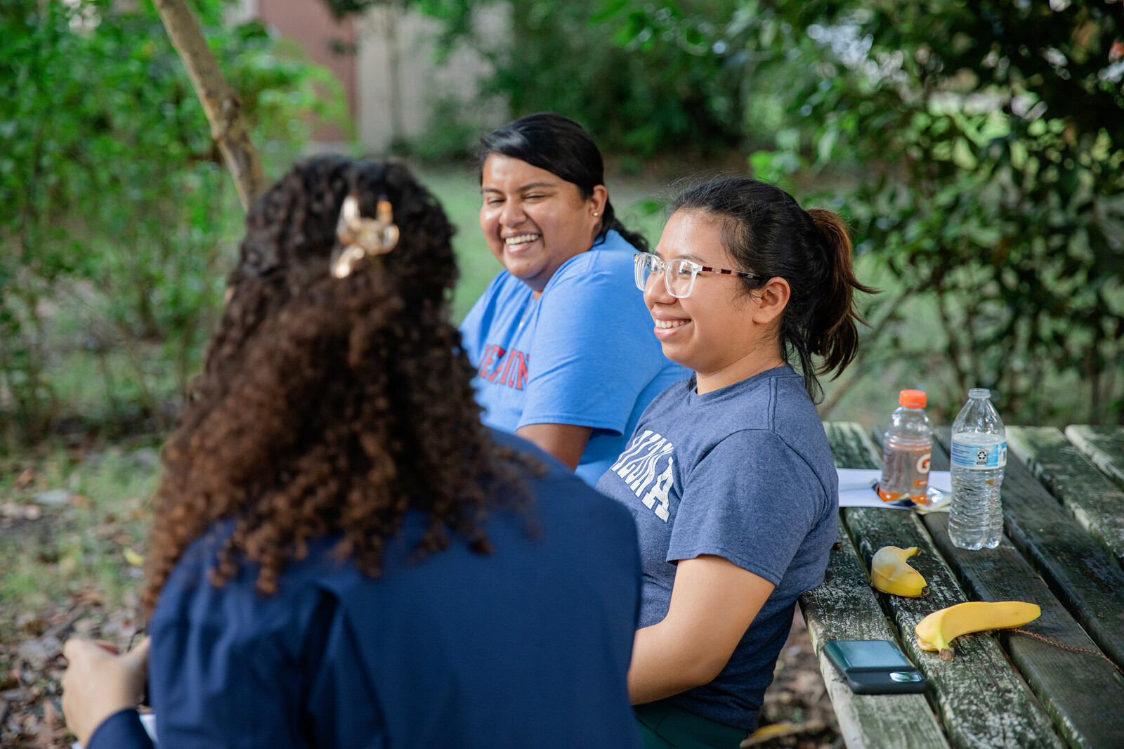 Three young people seated at a picnic table smiling and laughing