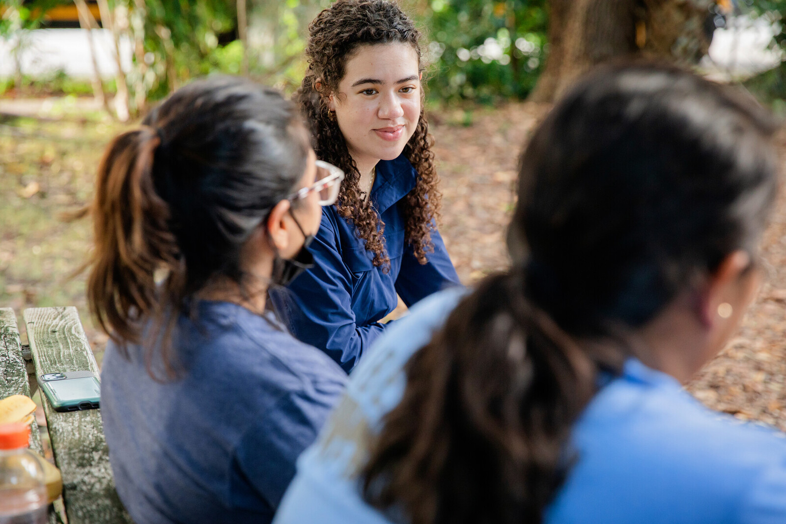 three young people talking on a park bench