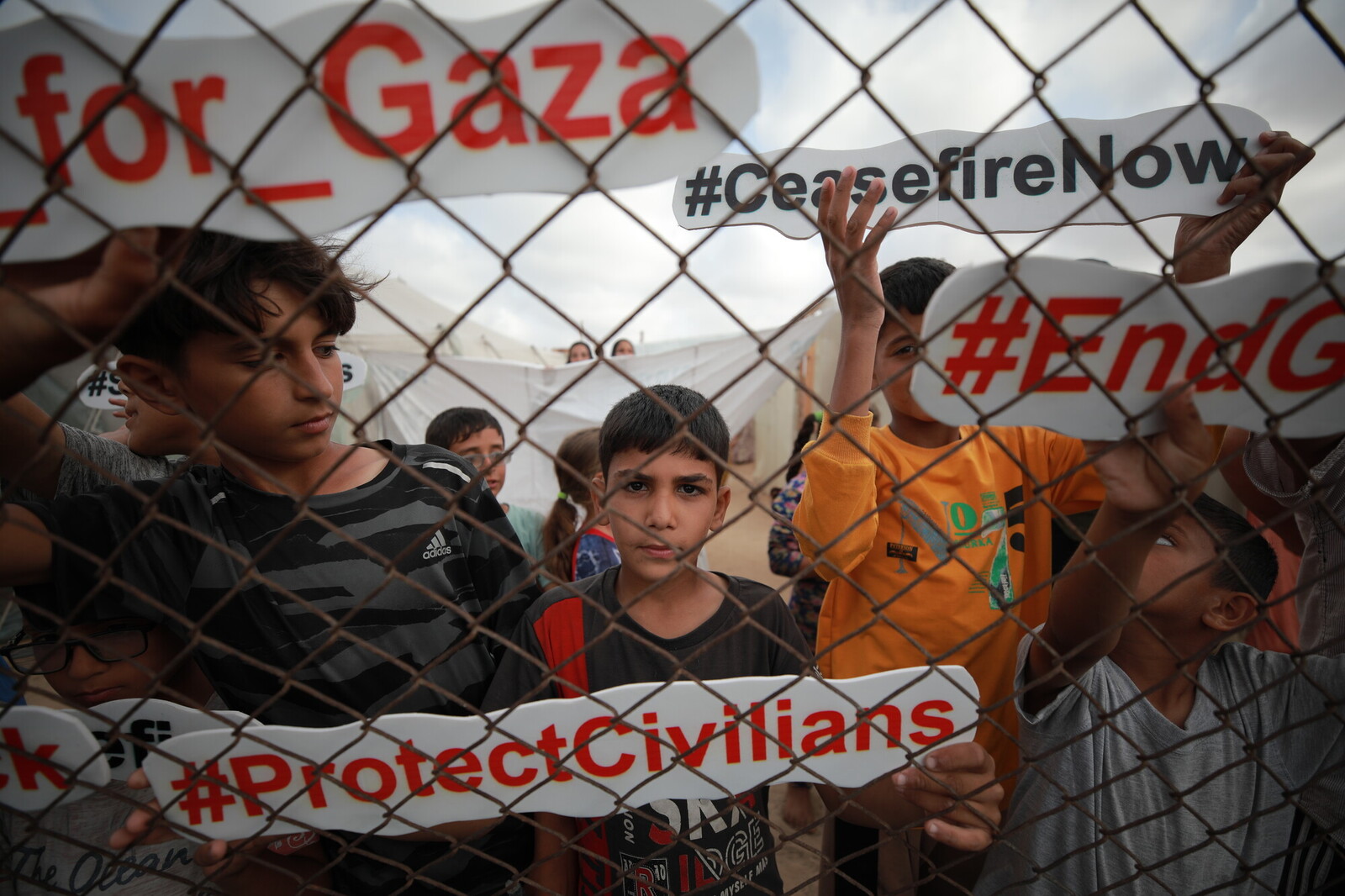 Children holds signs about Gaza behind a chain link fence