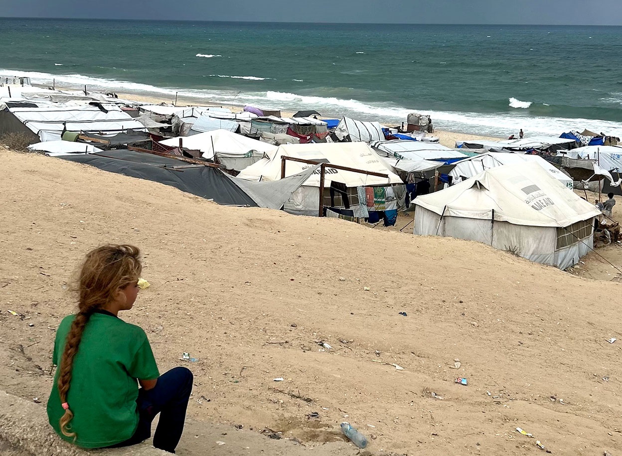 Girl sits on beach looking at tents near the water