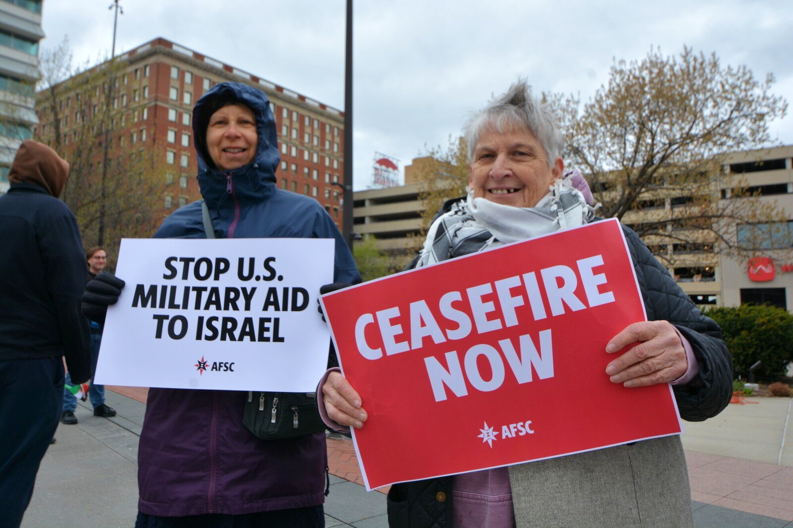 2 people hold signs that say Stop U.S. military aid to Israel and Ceasefire Now