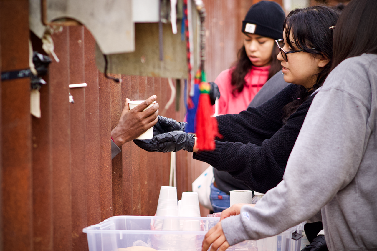 A person handing supplies to immigrants through the border wall