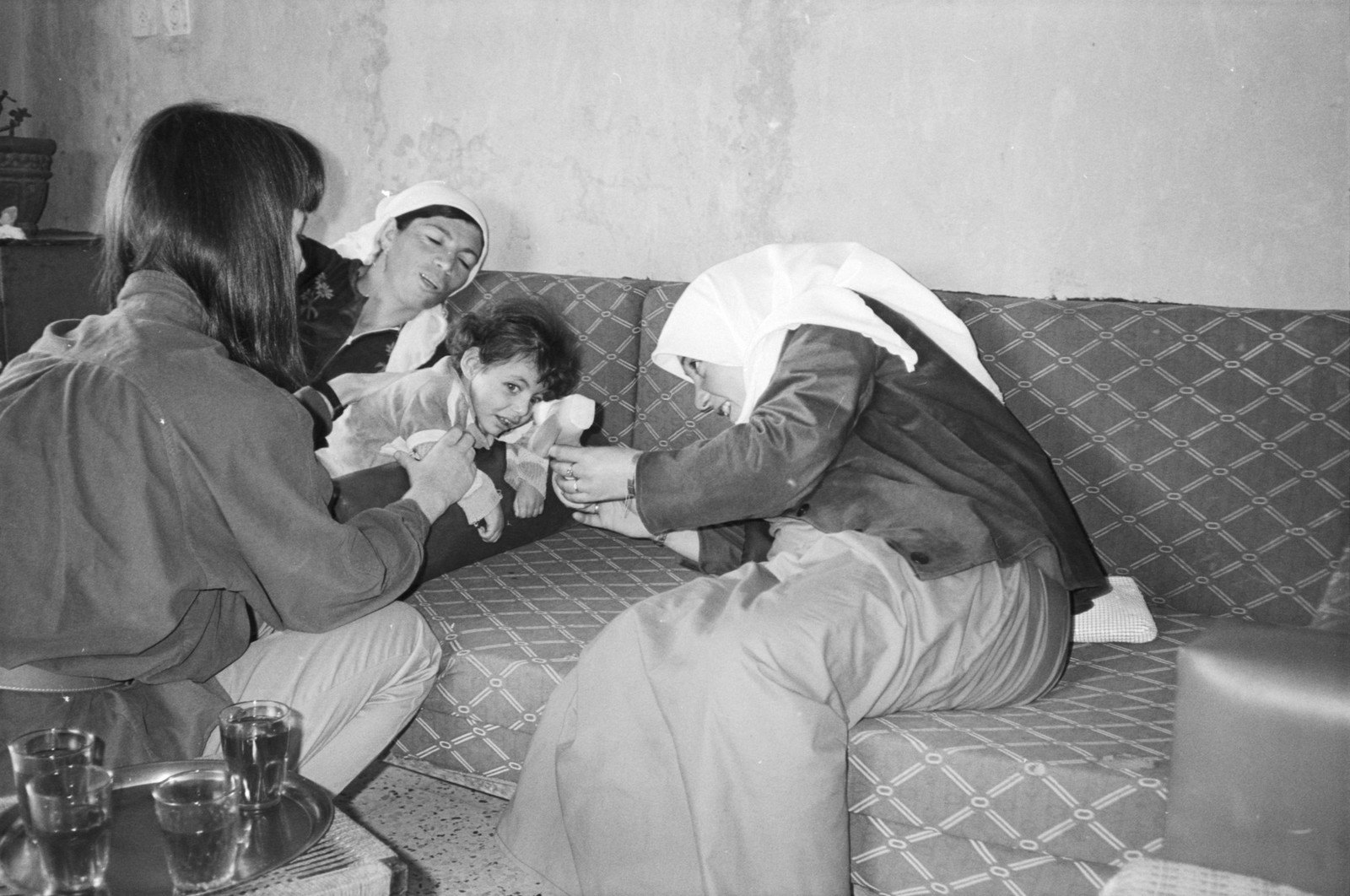 Three women help a young child on a sofa