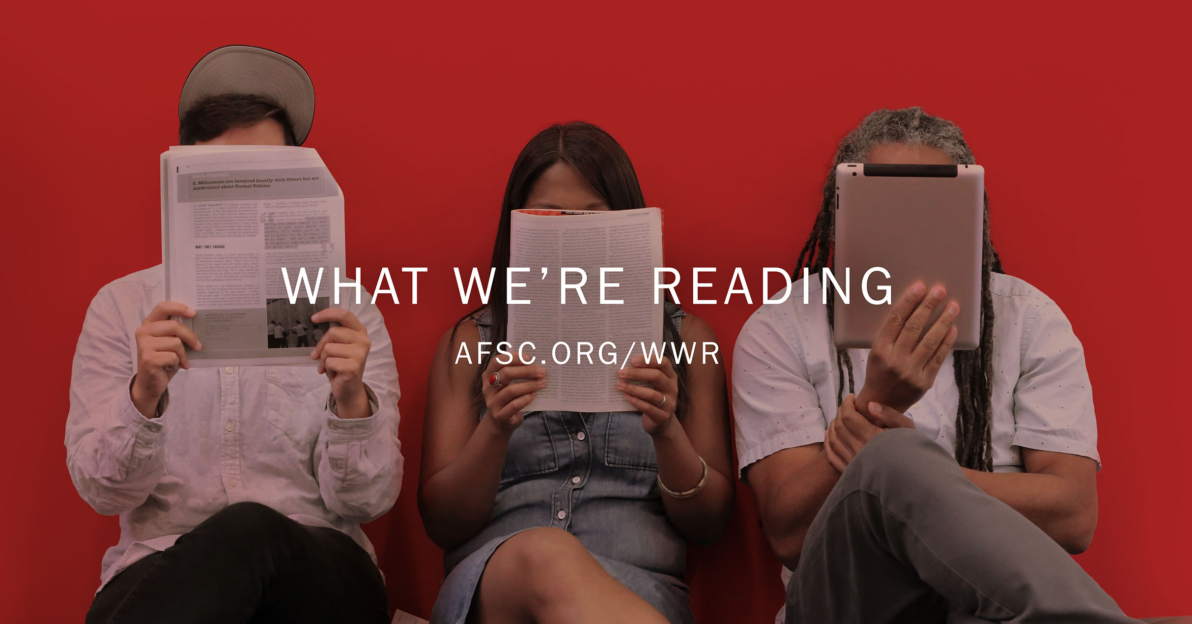 Three people sitting in front of a red wall reading iPads