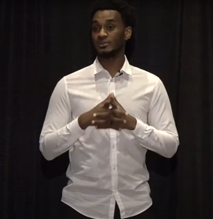 Joshua, wearing a white button-down, speaks to an audience.