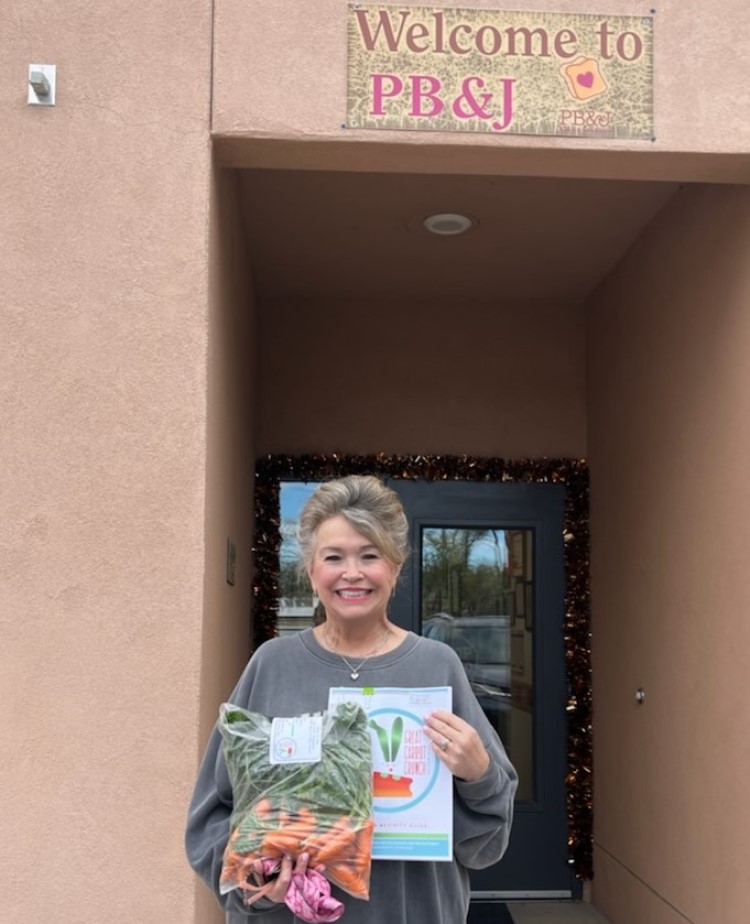 An older woman holds a bag of carrots and grins.